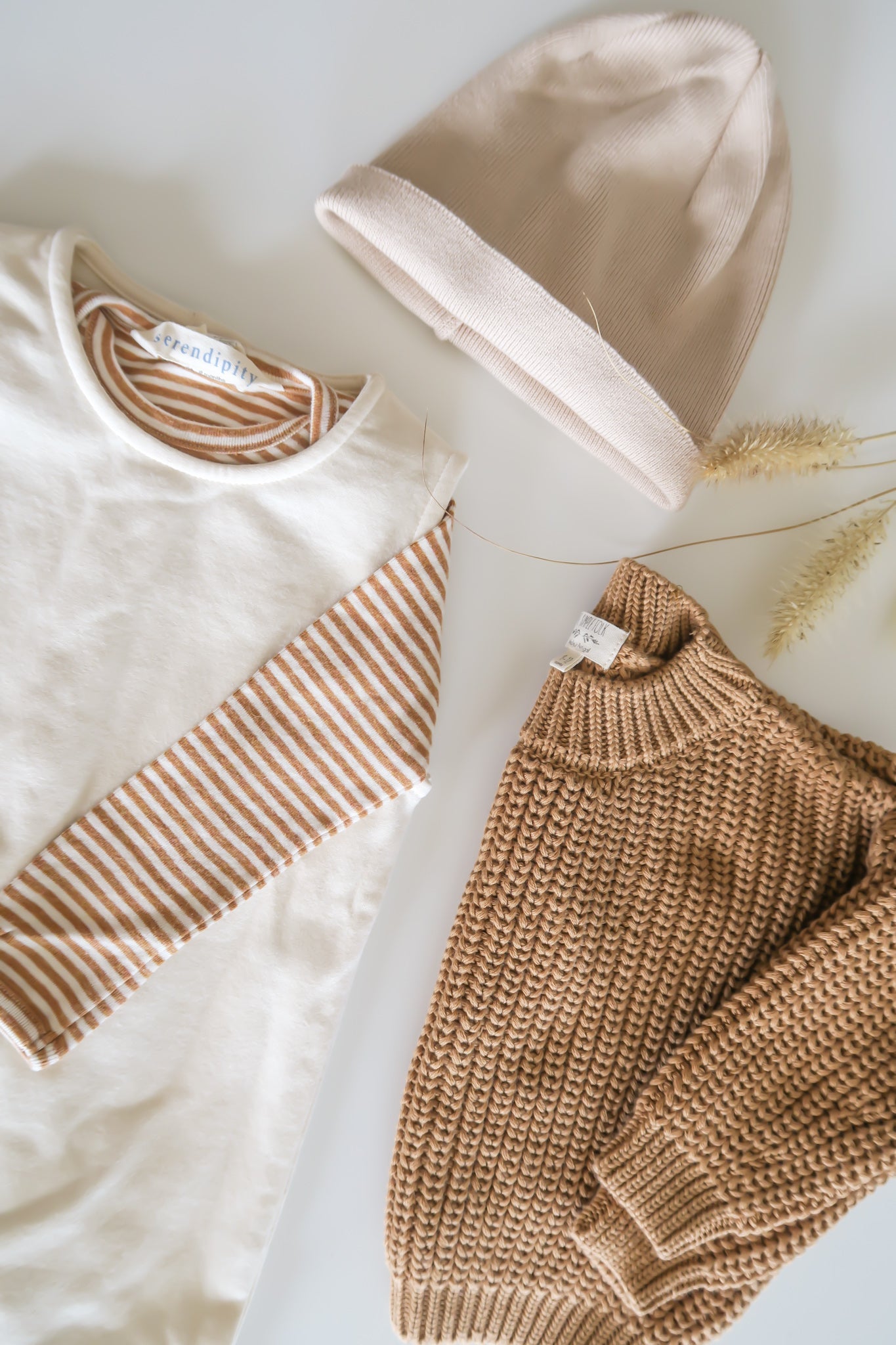 Organic baby clothes in brown from OiOiOi, beige and white with stripes lying on light background