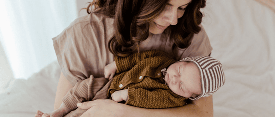 Brown haired woman holding baby wearing brown organic babyclothes from OiOiOi in her arms