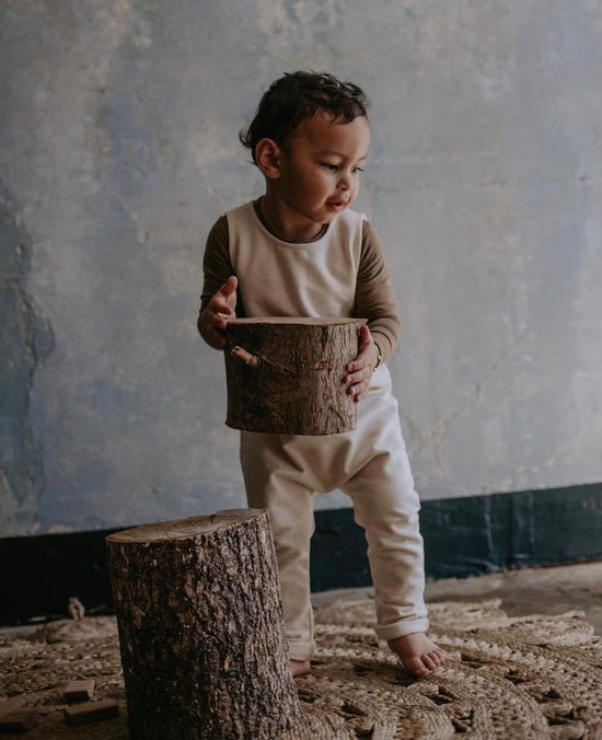 Child with dark hair and light organic cotton children clothes from The simple folk, carrying piece of sawed off tree stump